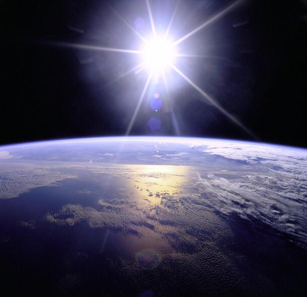 The sun rising above the Earth in space.