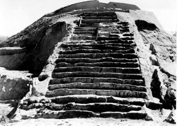 A massive stone structure with wide steps leading to its rounded top. Steps are mostly intact, while parts of the outer wall have broken off.