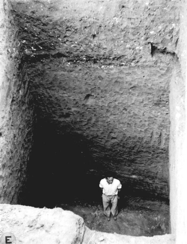 A man standing at a deep level of an excavation pit with flat squared walls.