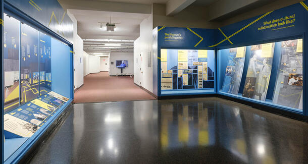 Glass display cases line a Museum hall which leads to an alcove with a video screen.