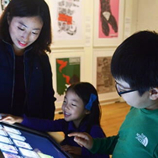 Cuban poster art is displayed on the walls and an adult and two children use an interactive touch screen in the center of the gallery.