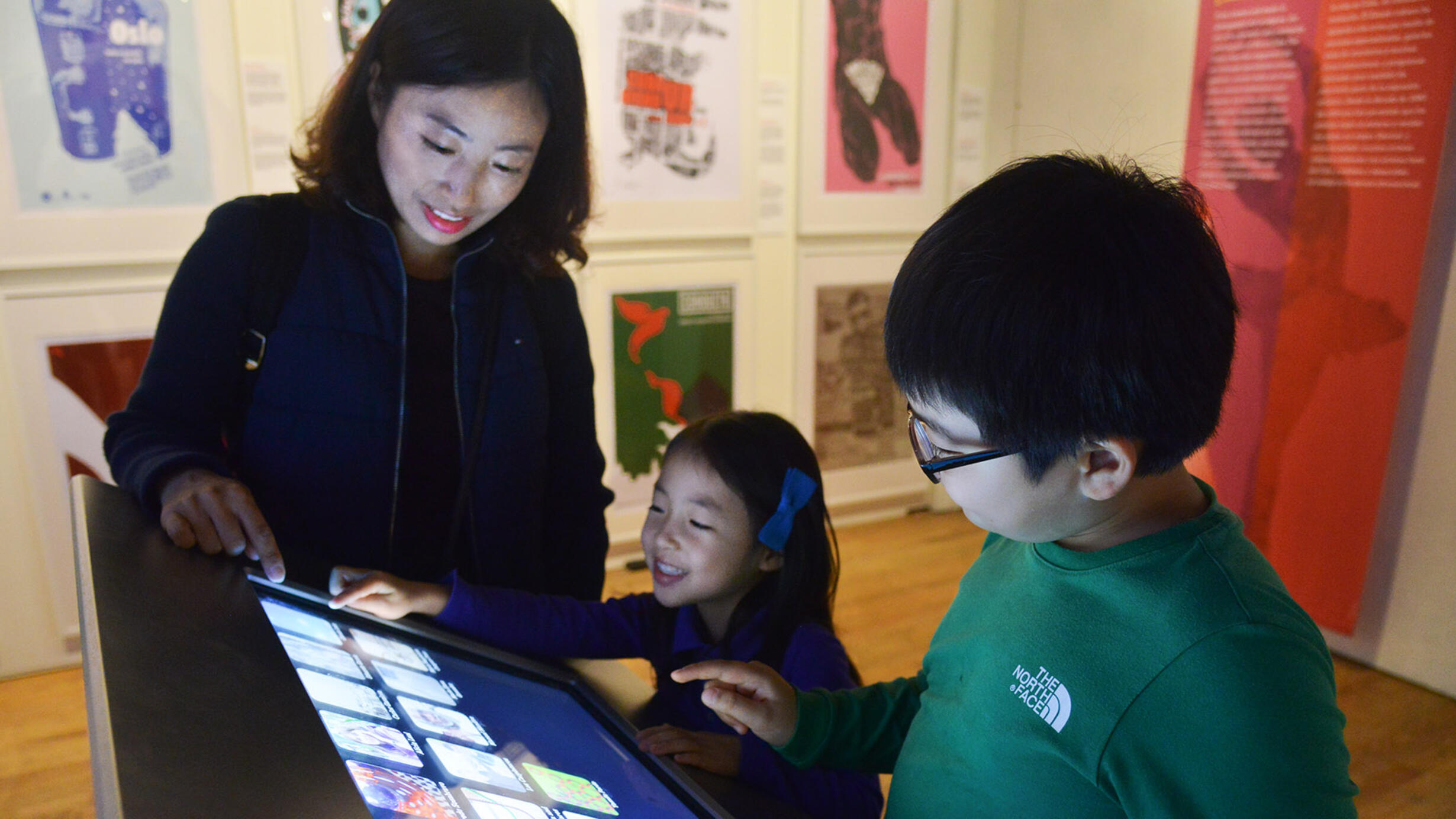 Cuban poster art is displayed on the walls and an adult and two children use an interactive touch screen in the center of the gallery.