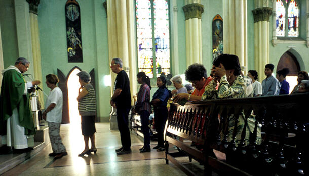 Line of people waiting to receive communion, stained glass windows in background.