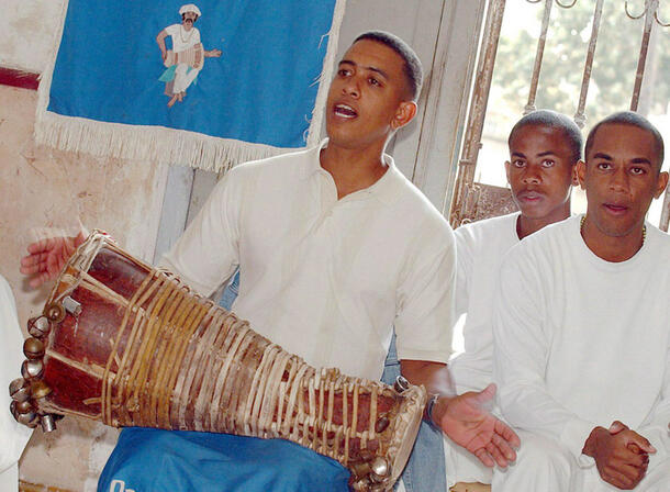 Man holds a batá drum and chants while two other worshippers stand nearby.