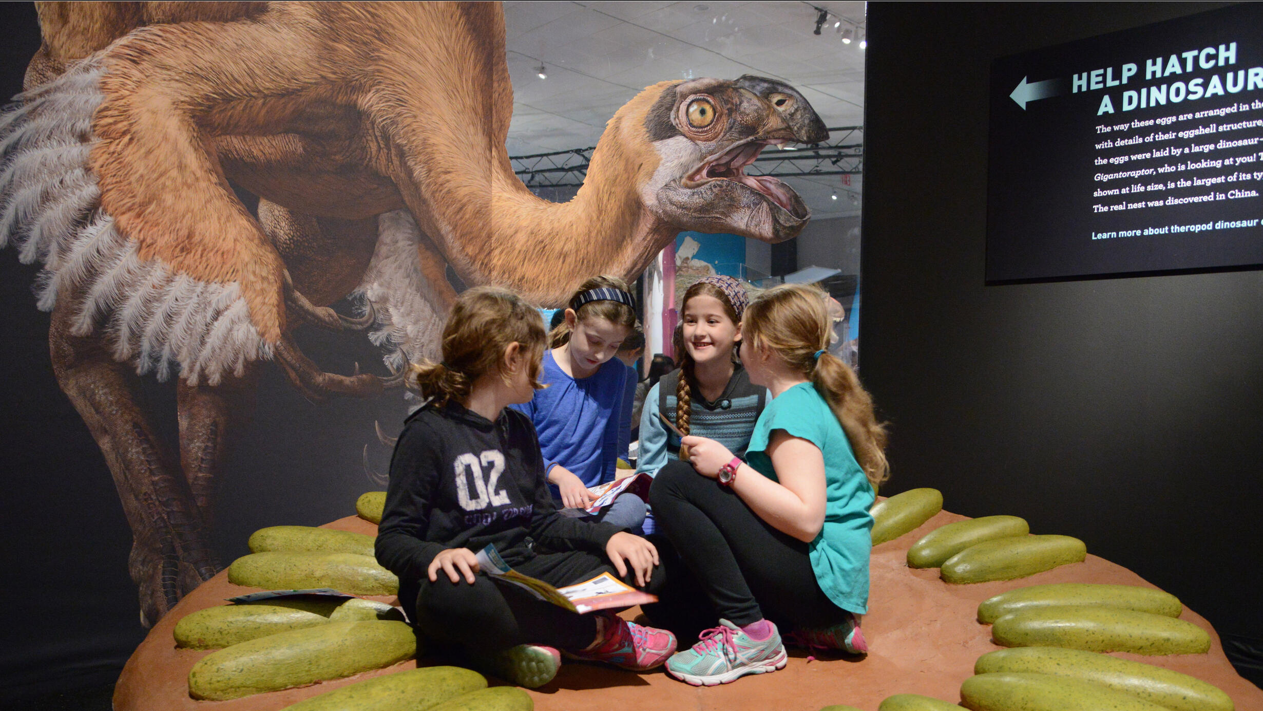 Four children sit at the center of a circle of life-size models of dinosaur eggs arranged in a circle.