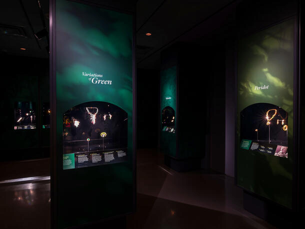 Interior view of Garden of Green special exhibition room, with wall text reading "Variations of Green" and "Peridot" over displays of jewelry.
