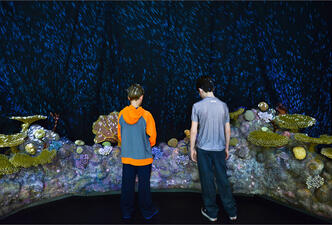 Two young visitors stand in front of a model of a section of the colorful Great Barrier Reef in Australia. 