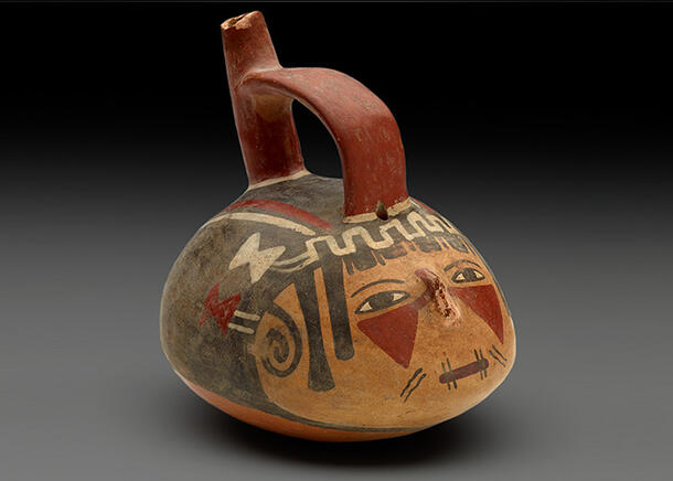 Rounded vessel in the shape of a human head has a face painted on it and is fitted with a handle and spout.