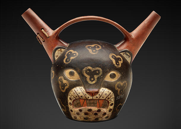 Ceramic jar is shaped and painted like the head of a jaguar with ears that are extended into spouts on either side of a handle.