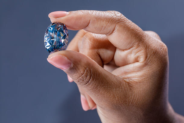 Large, egg-shaped blue diamond, known as the Okavango Blue, being held between a person's thumb and forefinger.