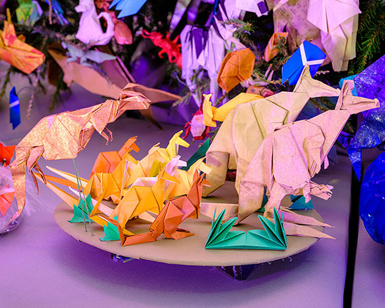 Ten kangaroo ornaments of varying sizes made with origami (folded paper) at the base of an artificial tree decorated with other paper ornaments.