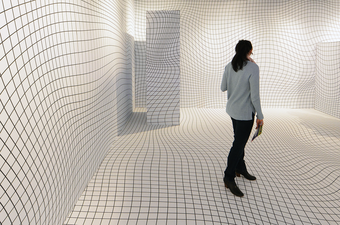 Person stands in a room in which the white walls and floors are covered in wavy black lines.