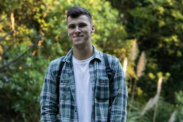 Artist Jordan Hill wearing a t-shirt and plaid button-up and standing outside. 