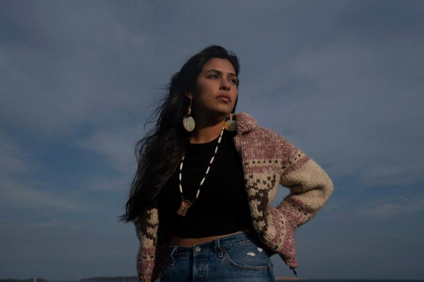 Artist Kayah George in a knit sweater, standing outside with open sky in the background.