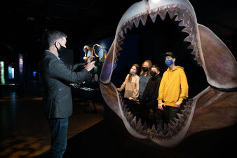 Four visitors stand inside the life-sized replica of the megalodon jaw, while another takes their photo.