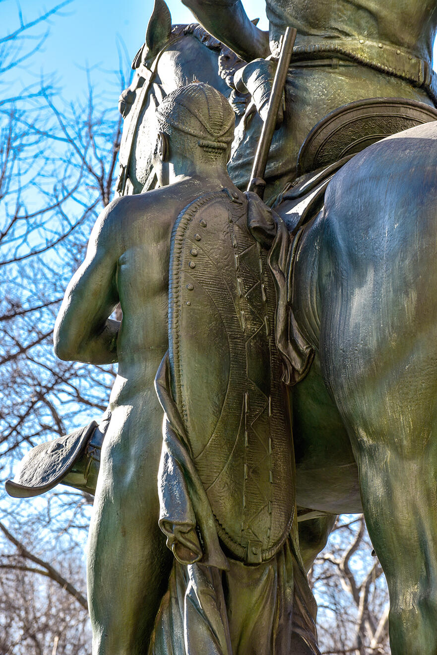 Detail of the back of the African figure in the Roosevelt statue, showing a long shield.