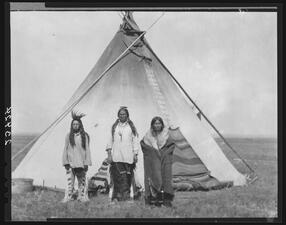 Three members of Blackfoot Nation stand in front of a tipi.
