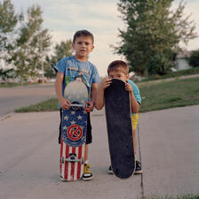 Two young Lakota boys stand holding skateboards.