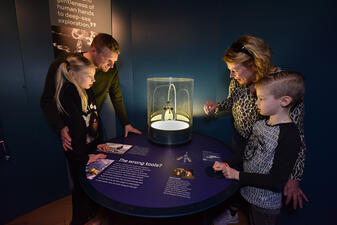 Four visitors stand around a table that houses "squishy fingers" in a glass display case.