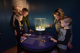 Four visitors stand around a table that houses "squishy fingers" in a glass display case.