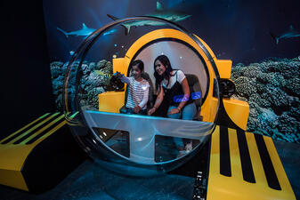Two Museum visitors sit inside a display of a triton submersible.
