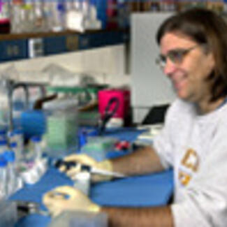 A man seated at a laboratory table and holding a pipette.