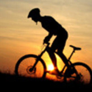 In silhouette, bicyclist in a helmet pedaling against a setting sun.