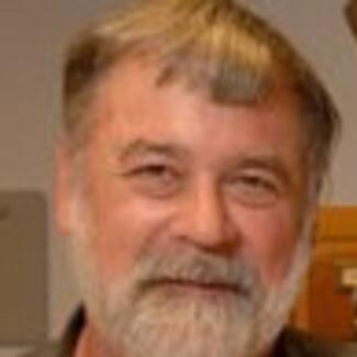 The head of a bearded man smiling at the camera, with a wood filing cabinet behind him.