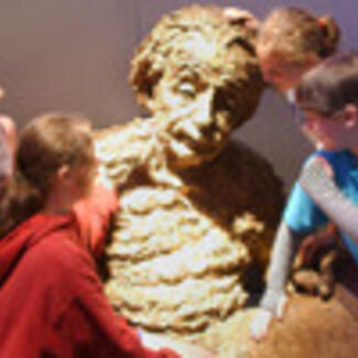 Four children next to a sculpture of a person,  Albert Einstein.