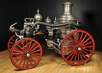 A steam fire engine such as were used circa 1896, and drawn by horses. This exhibition model has gleaming metal fixtures and red-colored spoke wheels.