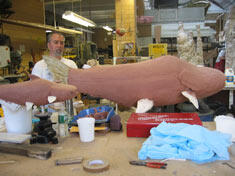 A man at a table with what looks like a huge model of a catfish in an early stage of construction.