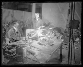 Two artisans view coral samples at a work table in the Museum workshop.