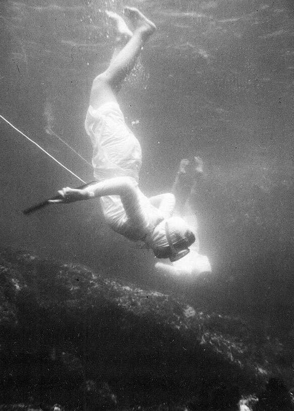 A diver wearing only a mask swims below the surface of the water, seeking pearls.