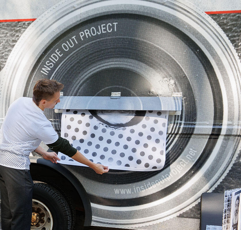 Inside Out Project team member pulls an oversized photographic print from an opening in the side of a photobooth truck.