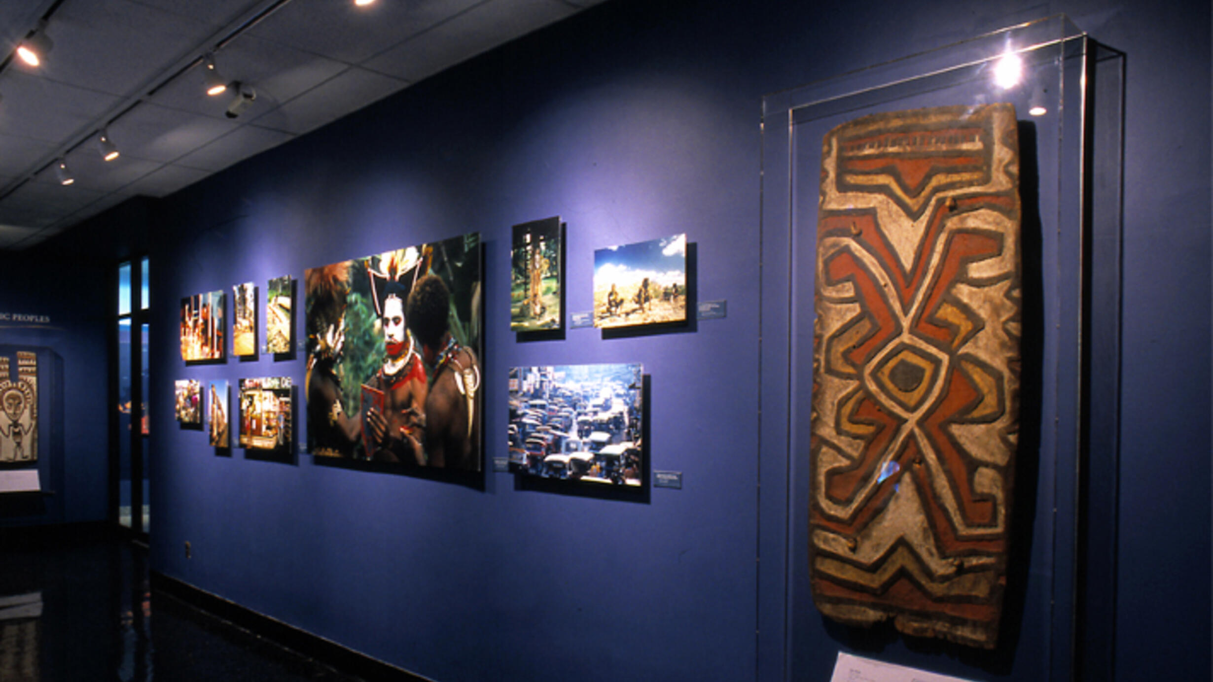 In the Museum’s Margaret Mead Hall of Pacific Peoples, a war shield of wood and paint from New Guinea. Also photos including one of Huli men in Papua, New Guinea applying ceremonial face paint.