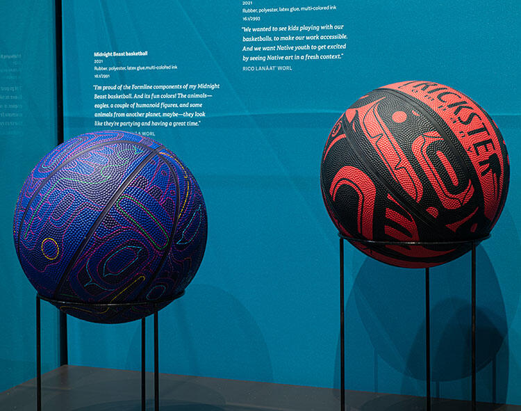 Two basketballs created with traditional designs, mounted side-by-side in a glass display case.