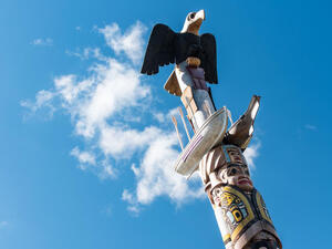 Top three figures of a carved wooden pole [from top to bottom]: an eagle, a canoe and longboat, a family.