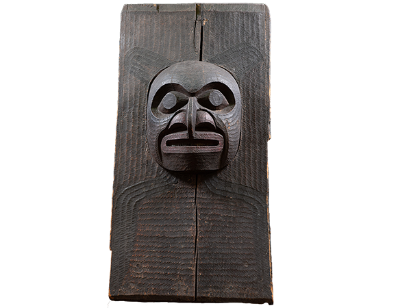 A striking carved face protrudes from a wood surface.