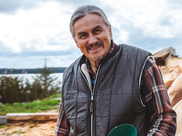 Man with gray hair and mustache in a flannel shirt and puffer vest poses outside.