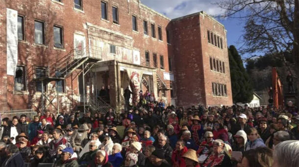 Crowds march past an old brick building.