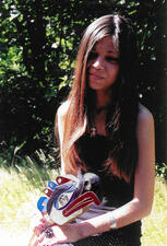 Woman seated outdoors holds a ladle carved from wood.