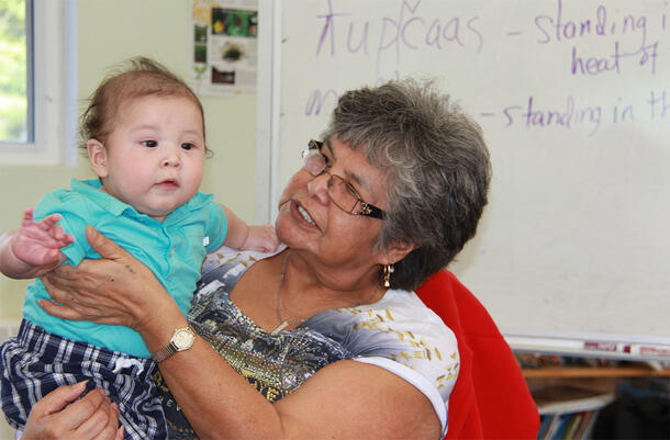 Georgina Amos holds a child on her lap. A white board with english and translations written on it is in the background.