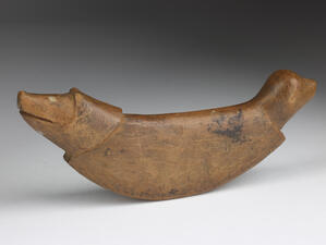 Curved wooden object with the ends carved in the shape of animals head and tail.