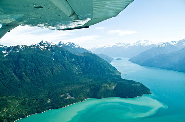 Aerial view of mountains and water, in view below the tip of a plane wing.