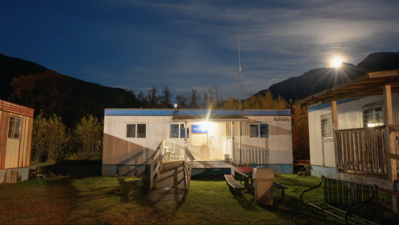 Shipping container building, flanked by two others, with a wooden ramp up to the door and a sign in front reading Nuxalk Radio. 