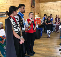 Person standing in a community space holds a microphone to speak with two people standing to her right.