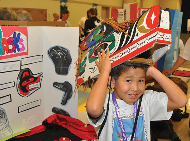 Child raises a cardboard replica of a headdress over his head.