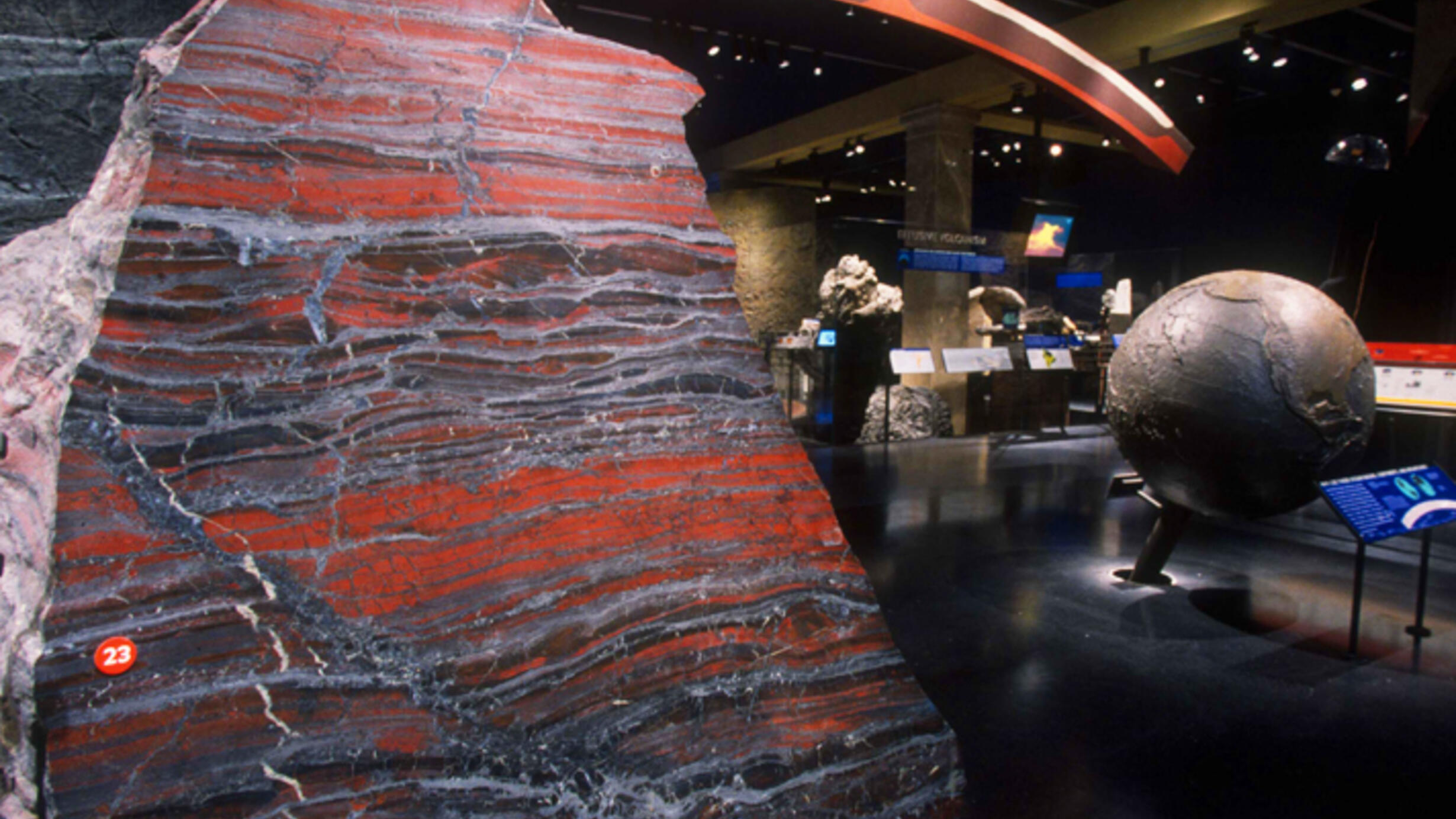 A large red-and-grey banded iron formation in a Museum hall.