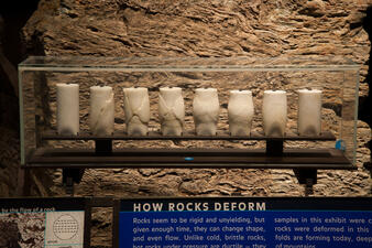 Eight cylinder-shaped samples of marble displayed from left to right in different states of deformation. An explanation panel states how rocks deform under heat and pressure.