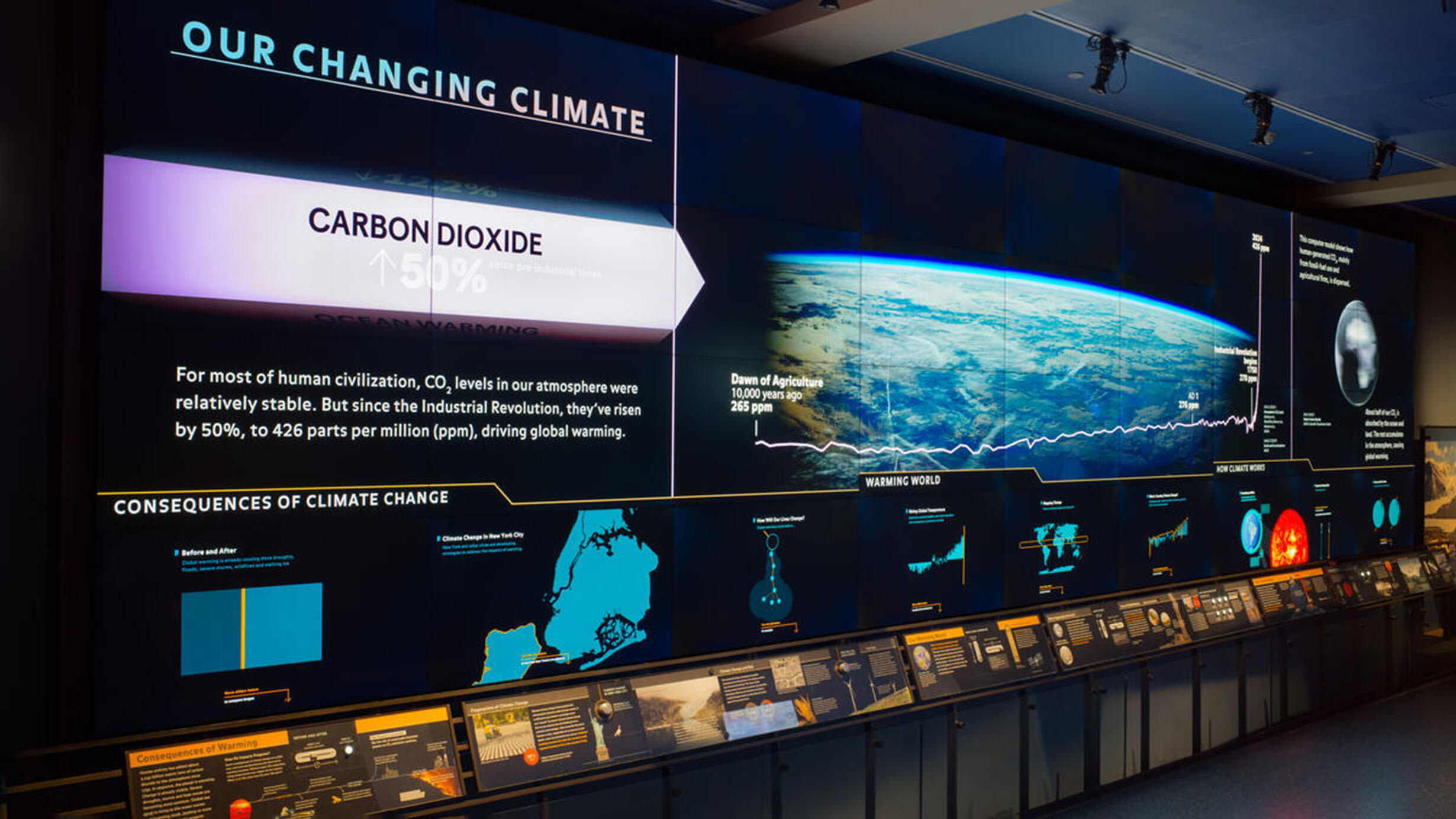 The digital climate change wall in the Hall of Planet Earth with text reading "Our Changing Climate" beside graphic of Earth from space.